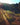 A dirt path winds through a grassy hillside, bathed in soft sunlight, leading into the distance.
