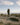 Person with guitar and backpack walking in desert under blue sky