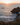 Sunset over ocean with rocky outcrop and lush coastal greenery